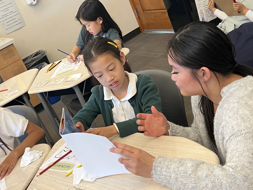 A camper writing during a classroom activity with a helper
