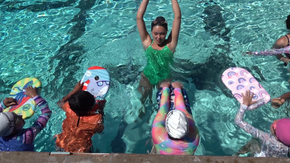 A camper doing a handstand in the pool surrounded by friends